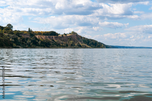 landscape of water, hills covered with trees and blue sky with clouds on summer river