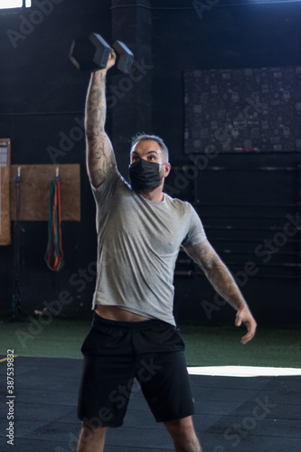 Chico con mascarilla en un gimnasio realizando Cross training con mancuernas