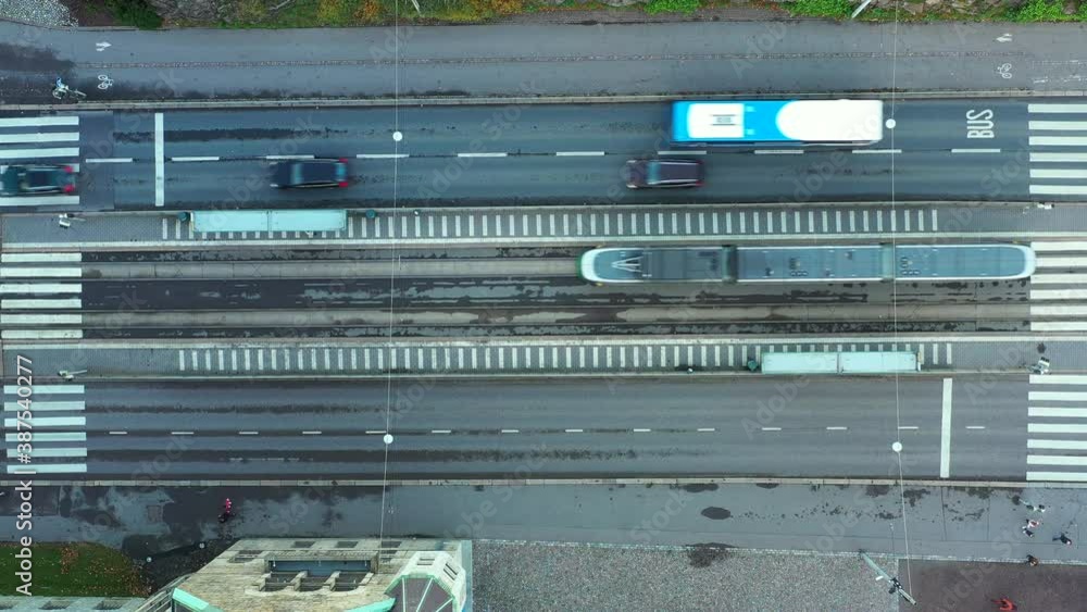 The tram is arriving at the stop on Helsinki street, Finland. Cars and busses are moving on the street. The tram is arriving at the stop on Helsinki street, Finland. Cars and busses are moving on the street.