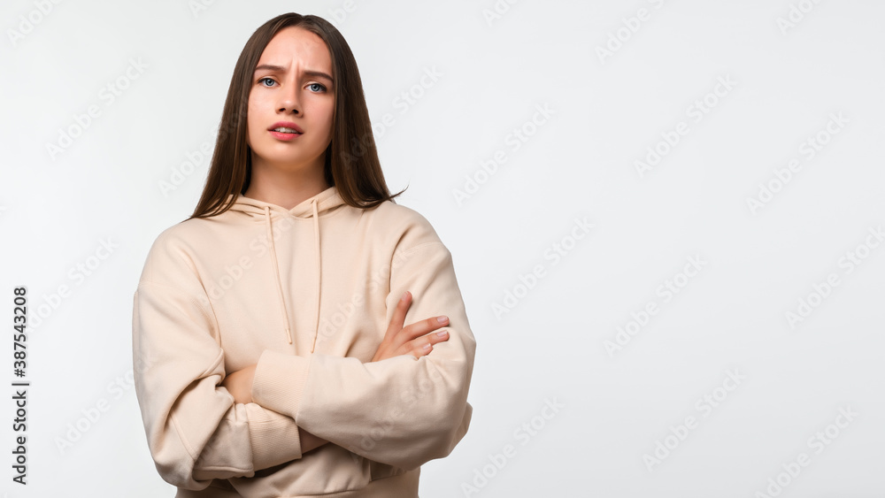 Fototapeta premium Photo of Offended girl posing isolated on white background. Holding hands crossed, looking at camera. Place for ad