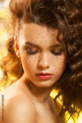 Creative winter makeup with golden snowflakes on her face and wavy hairstyle