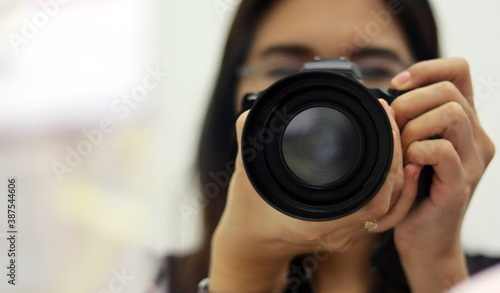Asian woman take a photo with mirrorless camera in studio, fashion modern photographer shooting portrait herself. Selective focus on camera blurred background has copy space, artist hipster concept.