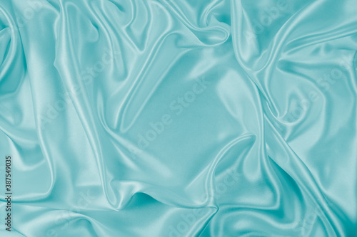 Photography of beautiful wavy turquoise silk satin luxury cloth fabric, abstract background design.