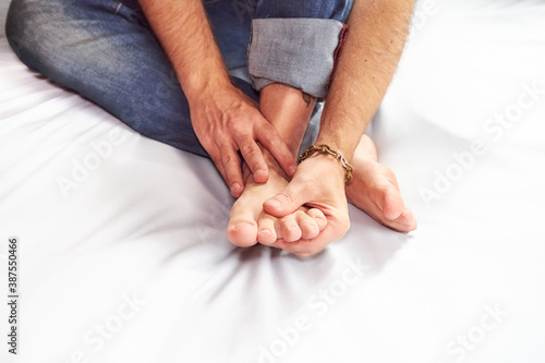 Man massage naked foot sitting on bed