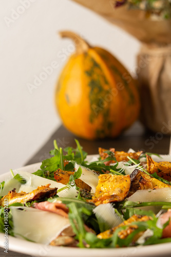 Light autumn salad with arugula, baked pumpkin, prosciutto and young parmesan, a plate of salad on a wooden table, chrysanthemums in a vase