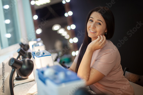 Beautiful woman tailor with long dark hair completing work with sewing machine at workplace