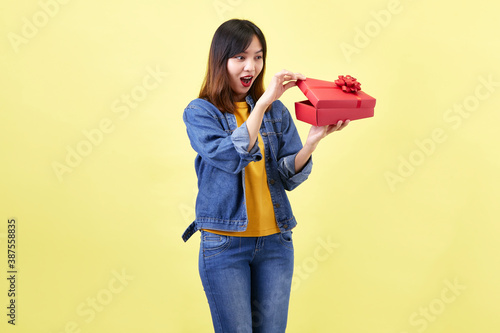 A beautiful excited young Asian woman in hand is opening a red gift