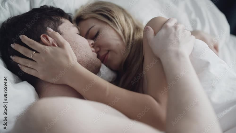 Romantic couple doing foreplay while lying in bedroom. Nude man and woman in bra in embrace enjoying intimacy and kissing. Affectionate lovers feel temptation and desire. Eroticism, passion. Romantic couple doing foreplay while lying in bedroom. Nude man and woman in bra in embrace enjoying intimacy and kissing. Affectionate lovers feel temptation and desire. Eroticism, passion.