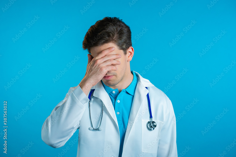 Frustrated doctor man in white wear over blue wall background. Doc is tired, bored of work, he disappointed, helpless Frustrated doctor man in white wear over blue wall background. Doc is tired, bored of work, he disappointed, helpless