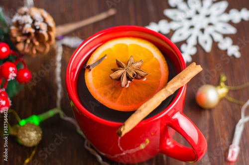 Delicious warm mulled wine with cinnamon, star anise and orange in red cup close-up on christmas background with copy space