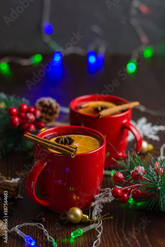 Aromatic, hot and delicious mulled wine with orange, cinnamon, star anise and cloves in red cups with Christmas decor. Feeling of celebration and warmth at home, vertical aspect ratio. © queen1987