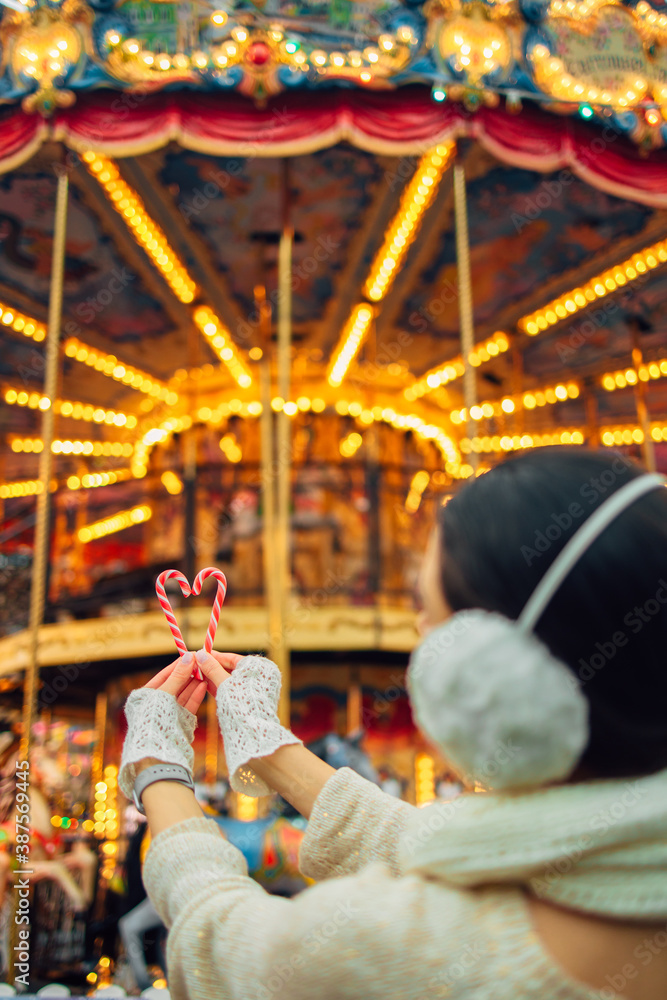 A girl holds a red striped Christmas two candy cane in the background of the lights of the Christmas market. New Year and Christmas symbols.