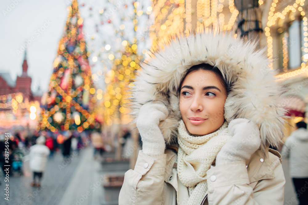 Girl in fur hood walking in Christmas market decorated with holiday lights in the evening. Christmas tree lights on background. Spending winter vacations in Red square, Moscow, Russia. Girl in fur hood walking in Christmas market decorated with holiday lights in the evening. Christmas tree lights on background. Spending winter vacations in Red square, Moscow, Russia.