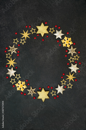 Christmas gold snowflake & star wreath with loose holly berries on grunge grey background. Abstract composition for the festive season.