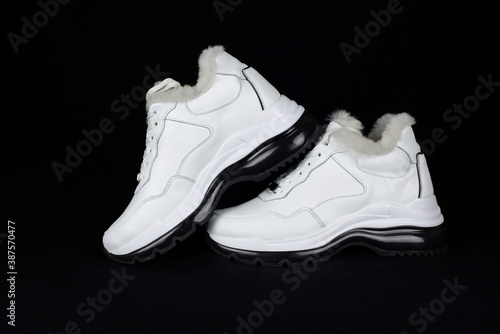 Women's white leather shoes with fur for walking in the cold season. Demi-season women's sports boots on a dark background