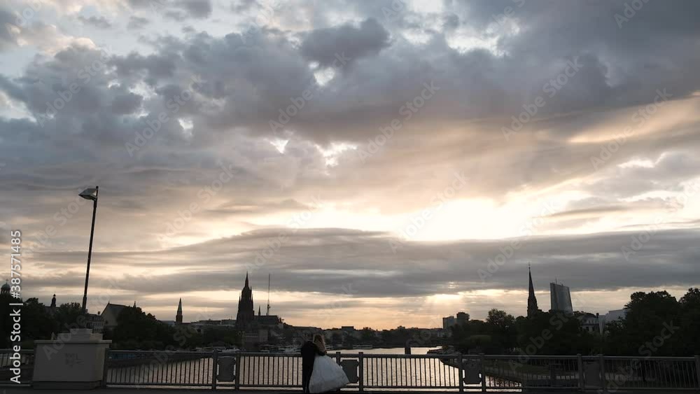 Happy wedding couple standing in Framfort on the bridge and enjoying the sunset over the river and the city Happy wedding couple standing in Framfort on the bridge and enjoying the sunset over the river and the city
