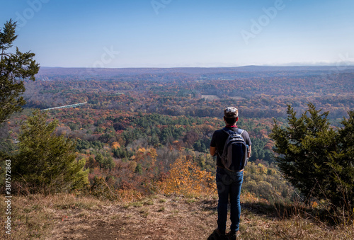 A lone man overlooks the Milford Bridge from a scenic point surrounded by brilliant fall foliage