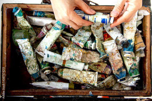 Painter hands picking oil paint tube from collection of neglected and messy artist oil paint tubes