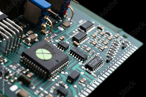 Green electronic circuit board with many electrical components against, isolated on black background
