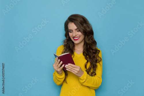 Smiling Woman In Yellow Sweater Holding Open Passport And Reading