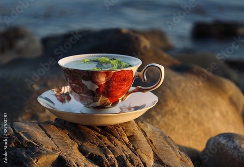 warm flower tea in a beautiful cup at sunset by the sea