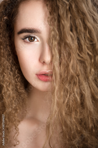 close-up portrait of a woman covering part of her face with curly hair. Vertical photo of a beautiful face