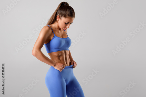 Fitness woman showing abs and flat belly, on gray background. Beautiful athletic girl, shaped abdominal