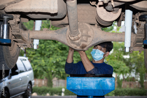 Mechanician changing car wheel in auto repair shop wearing a mask, coronavirus concept