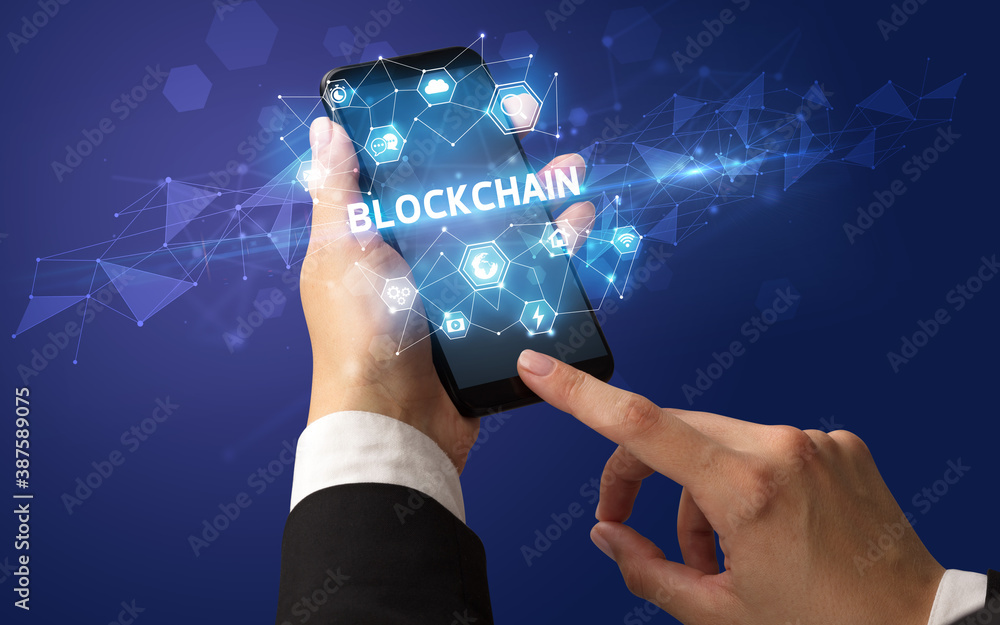 Female hand holding smartphone with BLOCKCHAIN inscription, modern technology concept Female hand holding smartphone with BLOCKCHAIN inscription, modern technology concept