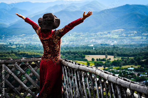 A woman wearing a red dress happily raised her arms in the mountains of nature. © Meawstory15Studio