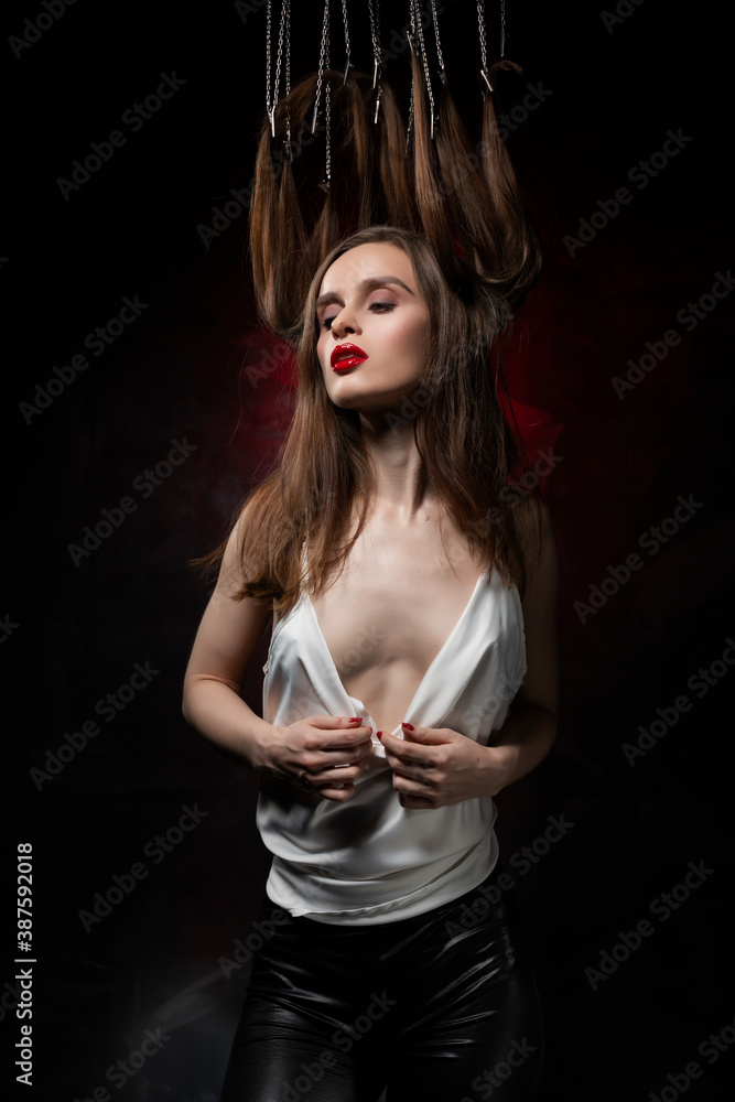 A beautiful girl with evening make-up and red lips wearing a blouse with a deep neckline and her hair suspended on chains, posing on a red and black background. Conceptual, avant-garde design A beautiful girl with evening make-up and red lips wearing a blouse with a deep neckline and her hair suspended on chains, posing on a red and black background. Conceptual, avant-garde design