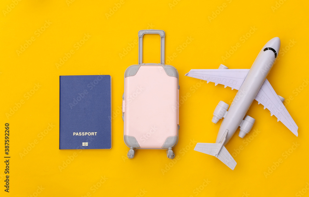 Travel flat lay. Mini plastic travel suitcase, air plane and passport on yellow background. Minimal style. Top view Travel flat lay. Mini plastic travel suitcase, air plane and passport on yellow background. Minimal style. Top view