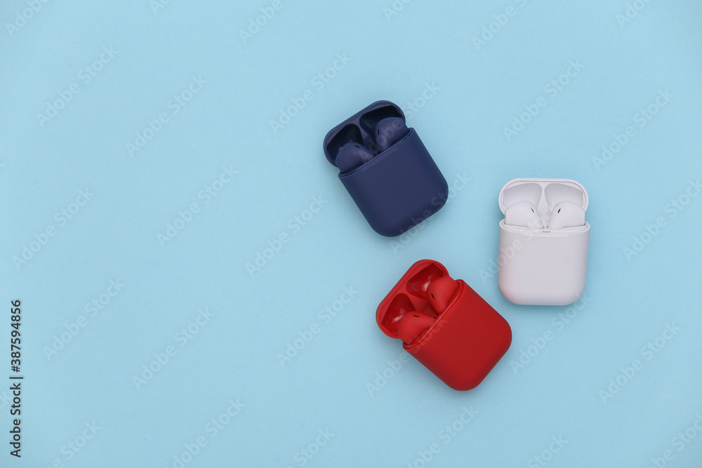 Different colors wireless headphones with charging case on a blue background. Top view Different colors wireless headphones with charging case on a blue background. Top view