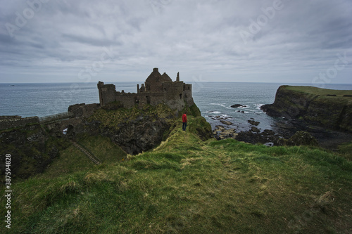 Young traveller standing in front of the dunluce dastle, cliffs and the sea at the coast of northern ireland