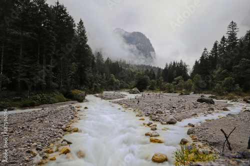 Long exposure of the WImbach river in the national park berchtesgaden, Bayern, Germany with fir trees and a mountain covered in clouds in background
