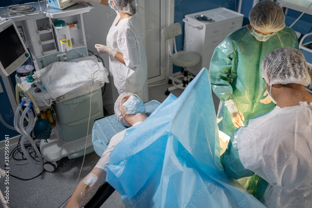 Patient lying on operation table while professional surgeons bending over him Patient lying on operation table while professional surgeons bending over him