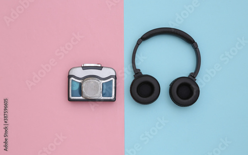 Mini audio cassette player with stereo headphones on a blue pink background. Top view