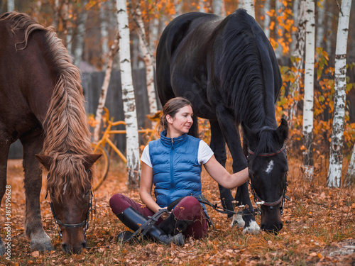 Two female riders sit on the grass next to the horses