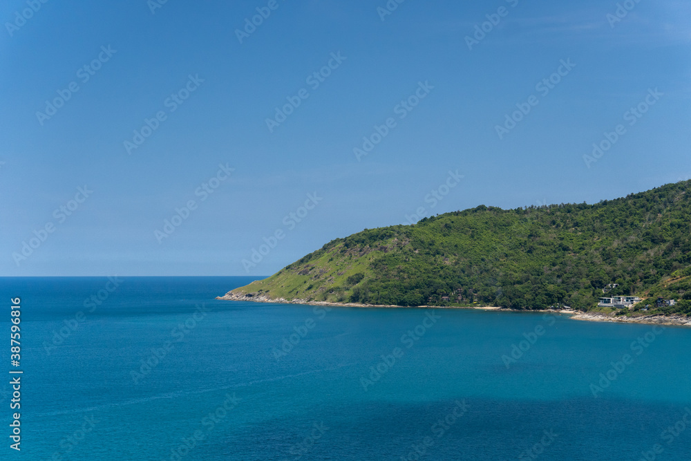 The seascape part of the island with the deep blue ocean and clear sky with the cliff full of forest tropical palm trees in the middle of summer holiday, famous tourist destination Phuket Thailand