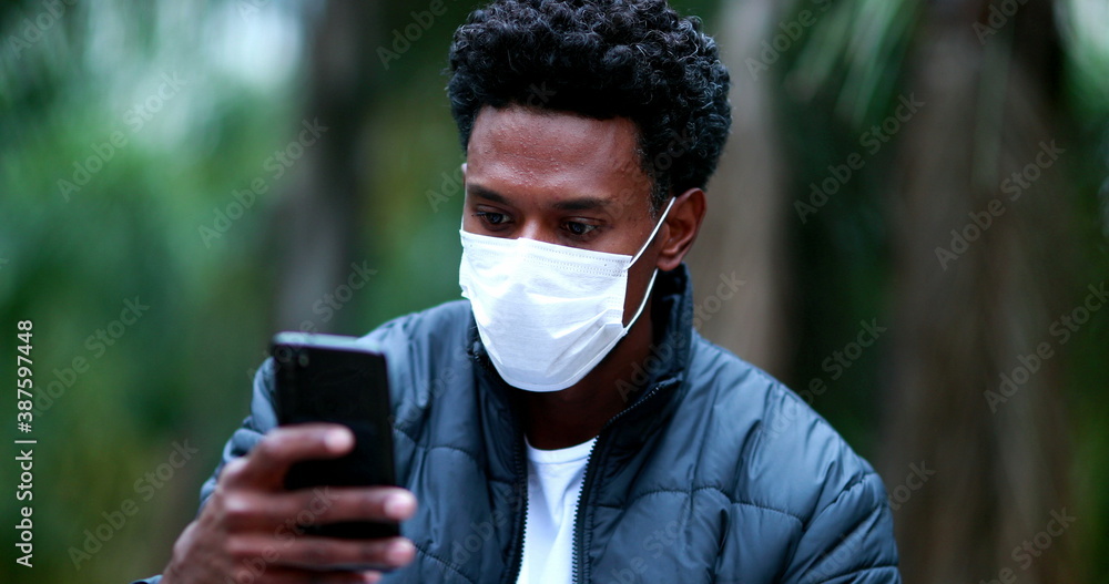Black african man checking cellphone wearing covid mask outdoors. Black african man checking cellphone wearing covid mask outdoors.