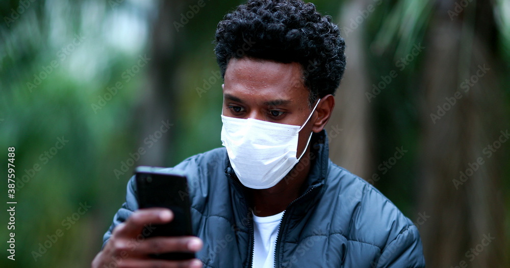 Black african man checking cellphone wearing covid mask outdoors. Black african man checking cellphone wearing covid mask outdoors.