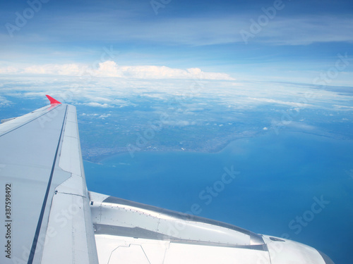 View from the cabin on the wing of an airplane flying in the sky. Beautiful white clouds, blue heaven, water and land down. Beautiful panorama of flight. Scene flight, traveling, trip, fly. Art idea