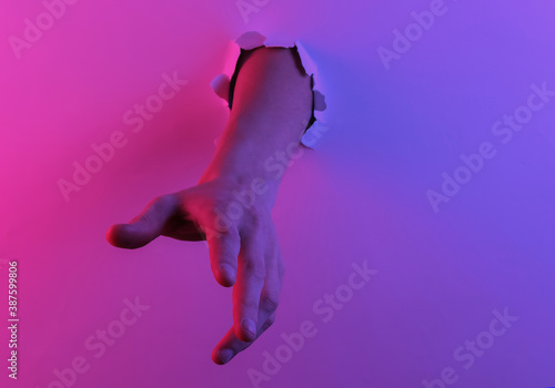 Mystical halloween concept. Hand through a torn hole. Creative pop art pink blue neon color. Trendy gradient illumination. Night light