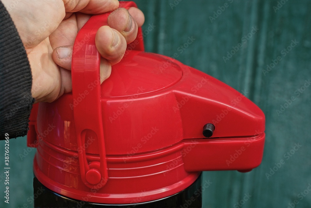 hand holds a large red thermos by the plastic handle on a green background hand holds a large red thermos by the plastic handle on a green background