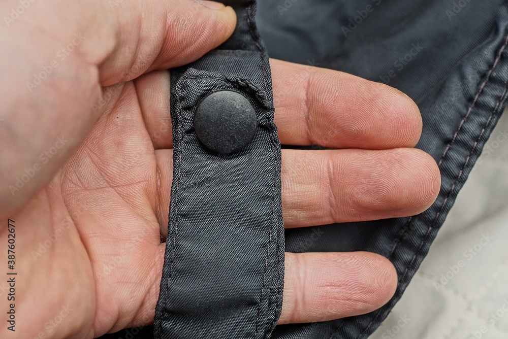 hand holds a black harness made of fabric with plastic rivet on the clothes