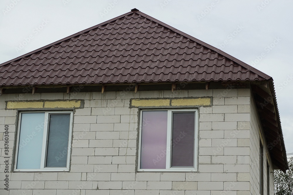 gray brick attic of a private house with two windows under a brown tiled roof on the street against the sky gray brick attic of a private house with two windows under a brown tiled roof on the street against the sky
