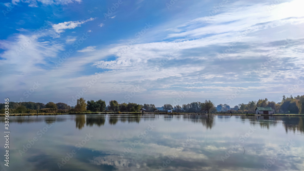 Fototapeta premium Sunny day on the perfect lake. Autumn lake with reflection on the water. Cloudy sky in the sunny day.