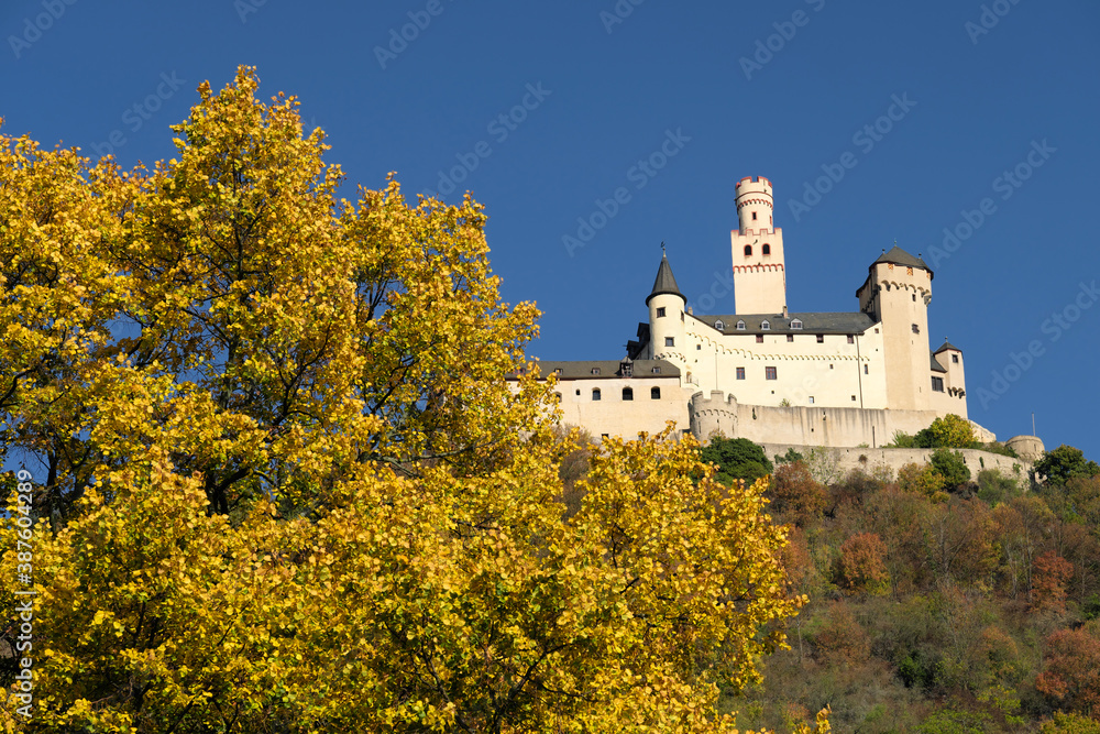 The German castle Marksburg on a mountain above the rhine and deep blue sky and a tree with yellow leaves in the autumn - Stockphoto 