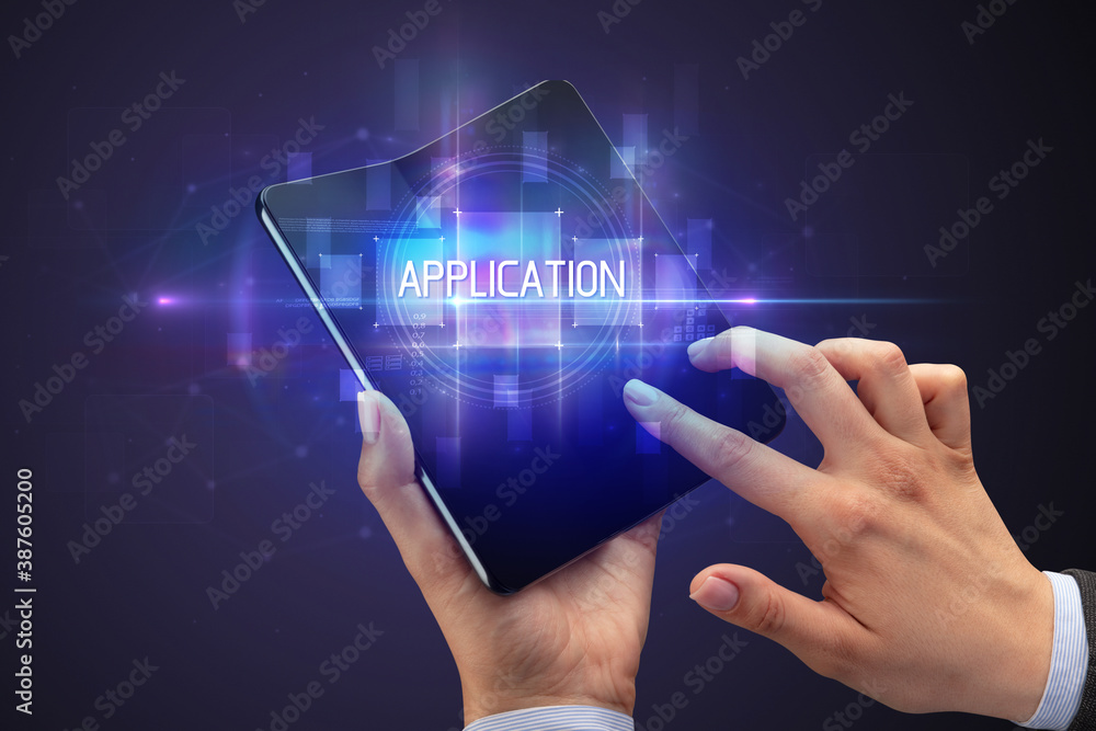 Obraz premium Businessman holding a foldable smartphone with APPLICATION inscription, new technology concept