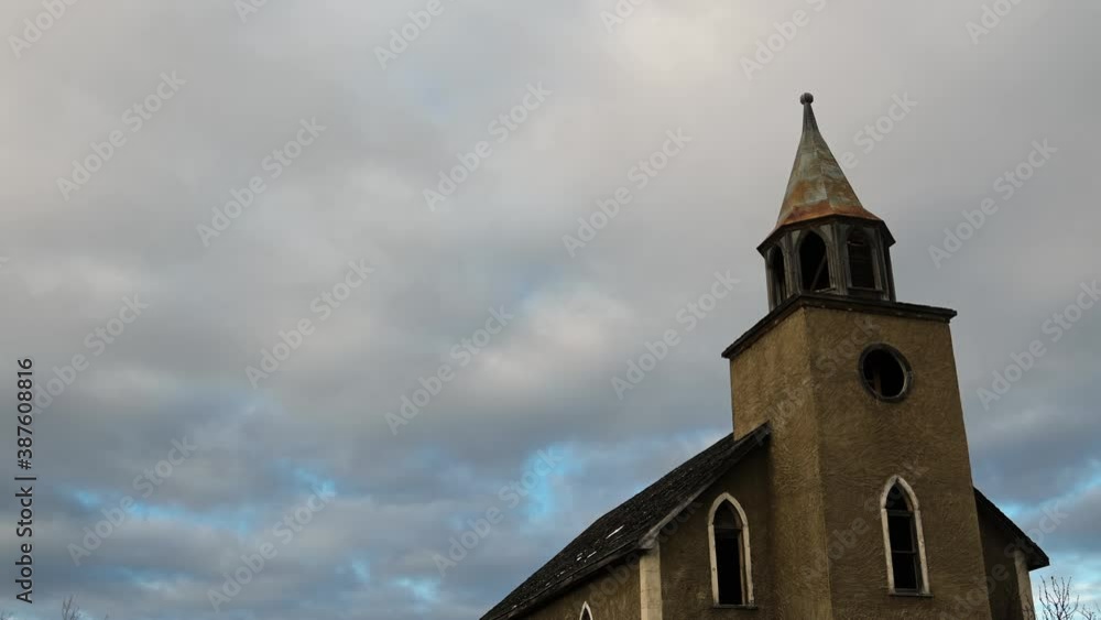 Looking up an old abandoned church with broken windows and a missing cross at white and gray clouds moving through the sky.
Looking up an old abandoned church with broken windows and a missing cross at white and gray clouds moving through the sky.